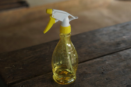 A close-up of a yellow spray bottle with a white nozzle, placed on a wooden surface. Ideal for cleaning tasks, gardening, or DIY projects in any home.の素材