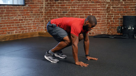 A young man engages in a mountain climber workout, showcasing athleticism and determination in a stylish fitness studio with a brick wall.の素材