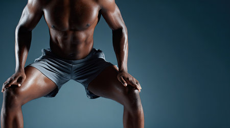 A muscular male athlete demonstrates strength and determination in an athletic pose. The dramatic dark background enhances the focus on his powerful physique and intense energy.の素材