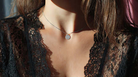 This captivating close-up features a woman's neckline adorned with a simple silver pendant necklace. The intricate lace top adds elegance, highlighted by soft natural light.の素材