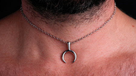 Close-up view of a silver pendant necklace worn on a male neck, showcasing intricate details against a dark background. Perfect for illustrating modern jewelry styles.の素材