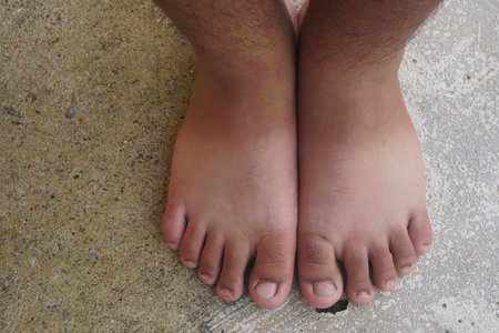 This close-up image showcases bare feet resting on a textured concrete surface, highlighting diverse skin tones and natural foot features in a relaxed, casual setting.の素材