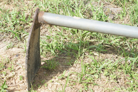 A detailed close-up of a worn shovel blade resting on the ground. The surrounding grass and soil highlight the tool's utility in gardening and landscaping projects.の素材