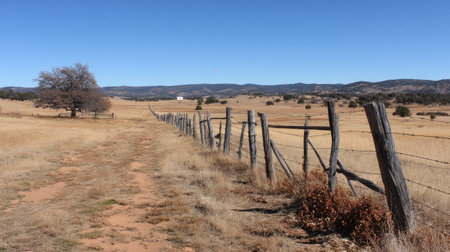Serene rural landscape featuring a rustic wooden fence, open fields, and a clear blue sky. A picturesque scene showcasing natural beauty and tranquility.の素材