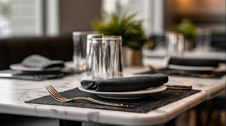 A beautifully arranged table in a modern restaurant featuring a black napkin, elegant fork, and sparkling glassware, creating a warm and inviting atmosphere.の素材