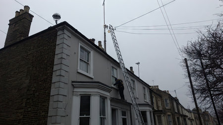 A technician climbs a ladder to perform maintenance on a building under a cloudy sky. This image captures urban service work, showcasing safety and professionalism.の素材