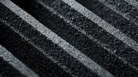 A detailed view of a textured black foam surface showcasing parallel grooves and a ribbed design, ideal for acoustic treatment and sound absorption applications.の素材