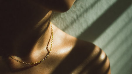 This detailed close-up captures the elegance of a gold necklace resting on a woman's neck, enhanced by a captivating interplay of shadows and soft light.の素材