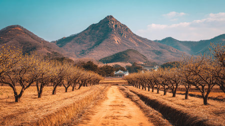 This captivating image showcases a winding dirt pathway leading through fruit trees, set against a stunning mountain backdrop under a clear blue sky.の素材