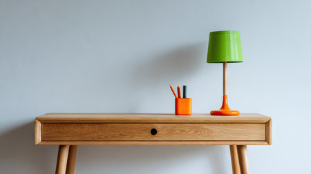 A stylish wooden desk featuring a minimalist design, accented by a green lamp and vibrant orange stationery, ideal for modern home or office spaces.の素材
