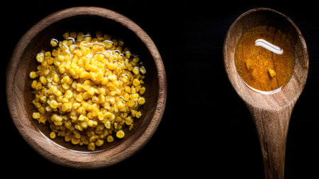 A close-up image of a bowl filled with vibrant yellow lentils alongside a wooden spoon, showcasing healthy cooking ingredients against a dark backdrop.の素材