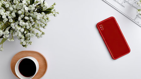 A beautifully arranged workspace featuring a vibrant red smartphone, a cup of coffee, and fresh white flowers, ideal for emphasizing creativity and focus.の素材