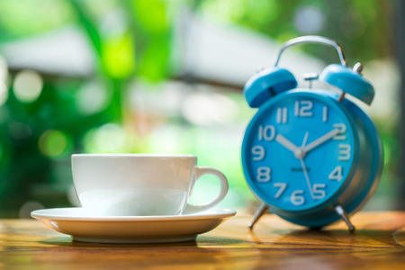 Cup of coffee with heart pattern in a white cup and blue clock on woodenの写真素材