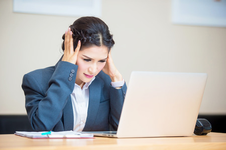 Businesswoman in office working with labtop,Woman Sitting at her Desk Massaging her Neck While Holding her Head.の写真素材
