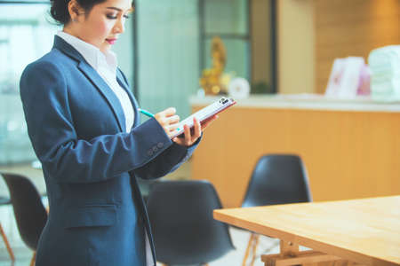Young businesswoman standing at workplace and reading paper in officeの写真素材