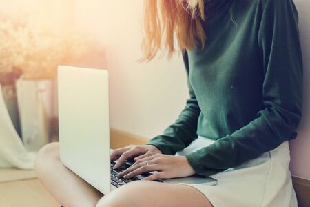 Happy casual beautiful woman working on a laptop sitting in the house on pink backgroundの写真素材