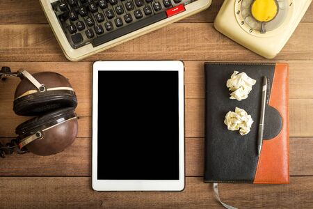 Top view of tablet with black space on the wood table with notebook, typewriter, old telephone and earphoneの写真素材