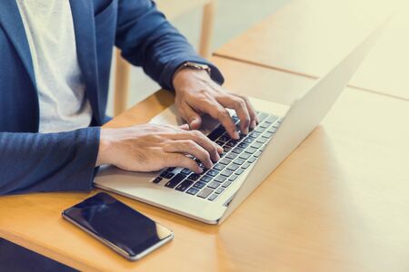 young man, wearing glasses and smiling, as he works on his laptop to get all his business done early in the morningの写真素材