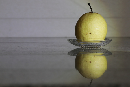 The yellow pear in glass cup and reflection on the groundの写真素材