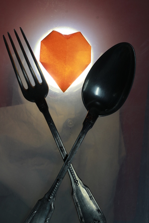 Transparency orange  paper heart with fork and spoon on red and white groundの写真素材