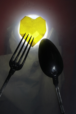 Transparency yellow  paper heart with fork and spoon on red and white groundの写真素材