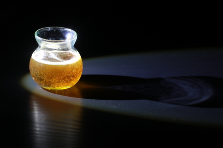 Side view of transparent honey bee in small glass cup on black backgroundの写真素材