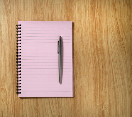 pink spiral notebook and a pen on the desk backgroundの写真素材