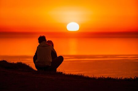 A red burning sunset over the sea with the silhouette of a young couple enjoying eveningの写真素材