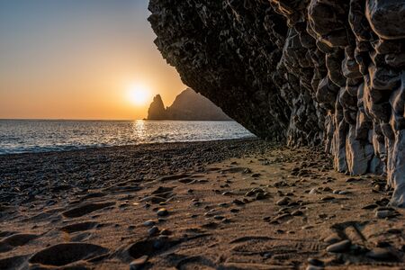 view of the sunset sea and the beach, the rock volcanic rock is lit by the warm sunset, sand and pebbles, volcanic basalt as in Iceland. Jasper beach, cape Fiolent, Crimeaの写真素材