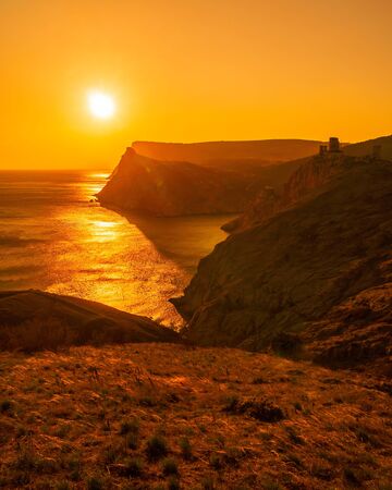 A red burning sunset with the silhouette of a cliff and old castle over the seaの写真素材