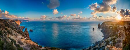 Panoramic seascape over the beach during sunset, with rocky cliff is lit by the warm sunset. Long exposure. Copy space. The concept of calmness silence and unity with nature.の写真素材
