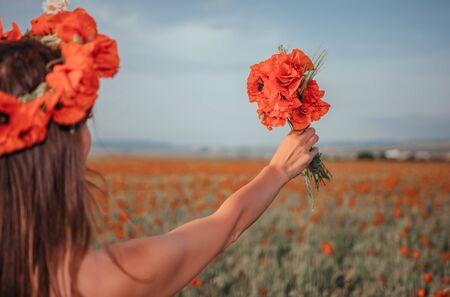 Bride in a white dress holding a bouquet of poppy flowers, warm sunset time on the background of the red poppy field. Copy space. The concept of calmness, silence and unity with nature.の写真素材