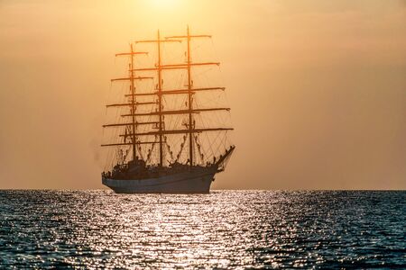 Seascape with sailing ship on sunset. Sailors set sails on masts of ship. White sailing vessel floating in the sea. Copy space. The concept of calmness, silence and unity with nature.の写真素材