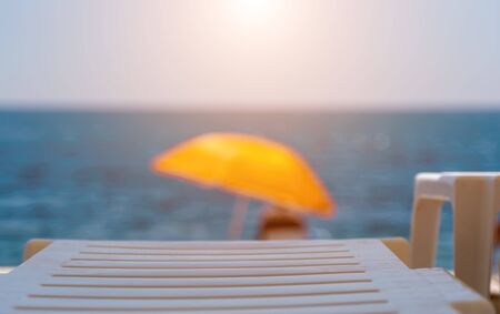 Summer vacation destination. Straw sunshades and sunbeds on the empty rocky beach with sea in the...