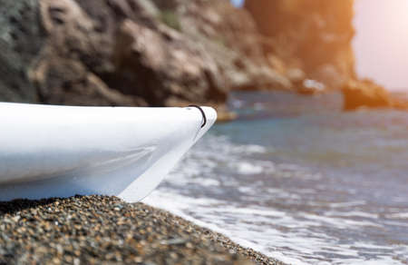 White kayak on an isolated pebble beach against the backdrop of rocks in the sea. Copy space. The concept of travel, relaxation, active and healthy life in harmony with natureの写真素材