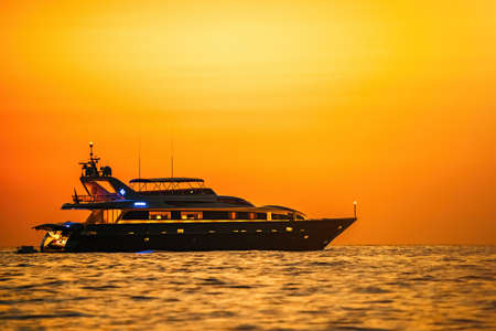 Golden romantic sunset on private modern luxury yacht anchored at sea - luxury holidays and travel concept. A red burning sunset over the sea with the silhouette of a fashionable yachtの写真素材
