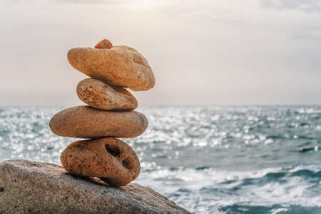 Balanced Pebbles Pyramid on the Beach on Sunny Day and Clear Sky at Sunset. Blue Sea on Background Selective focus, zen stones on sea beach, meditation, spa, harmony, calm, balance concept.の写真素材