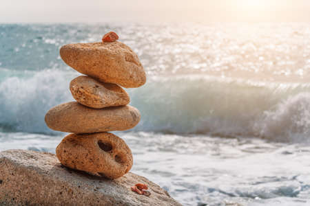 Balanced pebble pyramid on the beach on a sunny day. Sea foam on the background. Selective focus. Zen stones on the sea beach, meditation, spa, harmony, calmness, balance conceptの写真素材