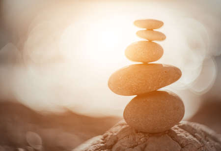Balanced Pebbles Pyramid on the Beach on Sunny Day and Clear Sky at Sunset. Blue Sea on Background Selective focus, zen stones on sea beach, meditation, spa, harmony, calm, balance concept.の写真素材