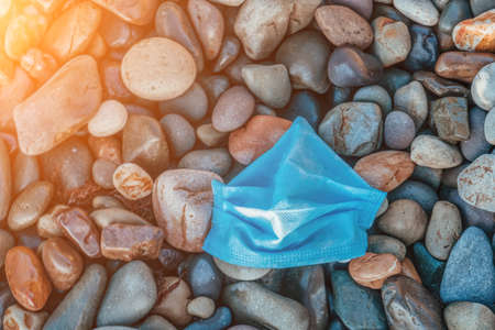 Close-up used Face mask on pebble beach, have started polluting water bodies since Covid-19 pandemic outbreak. Masks Are Polluting Beaches and Oceans. Coronavirus crisis leading new pollution.の写真素材
