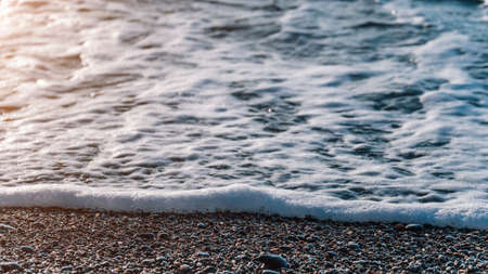 Selective focus. Sea foam on water surface in motion blur with bokeh lights from sunrise. Abstract...