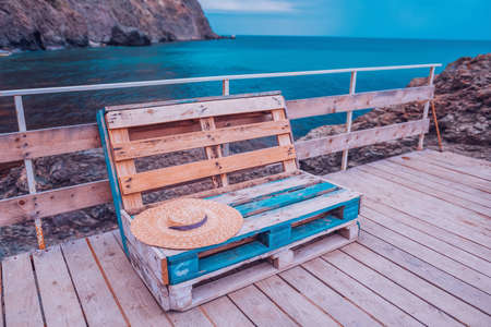 Beautiful look out on the ocean with pellet seats. Wooden bench made of pallets of freight cargo cases for sitting. Creative outdoor cafe benches Modern urban loft design Furniture from vintage boardsの写真素材