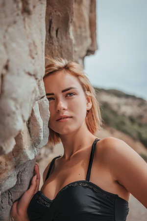 Young woman in black bikini posing on a sand rocks near the sea. Attractive young girl model posing on black sand volcanic beach on Baliの写真素材