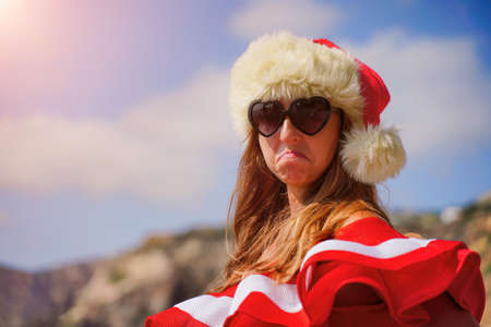 Young brunette woman in red swimsuit and Santa hat, swimming on kayak around basalt rocks like in Iceland. Back view. Christmas and travel conceptの写真素材