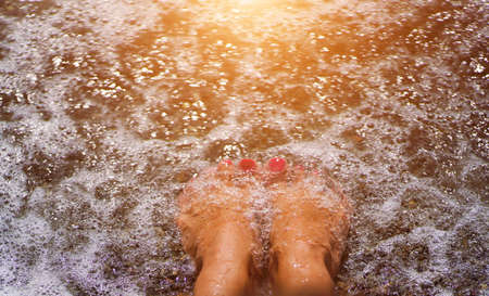 women's legs with a bright pedicure in the sand on the beach. summer holidays at seaの写真素材