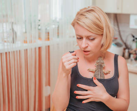 Pets, morning, comfort, relaxation and people concept. Happy young blonde woman with her domestic lizard, Bearded dragon or Pogona vitticepsの写真素材