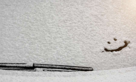 Snow background. Texture of wet snow with a cheerful smiley symbol pattern in the winter window of the car outdoors close-up. Smile in the snow, happy cheerful image.の写真素材