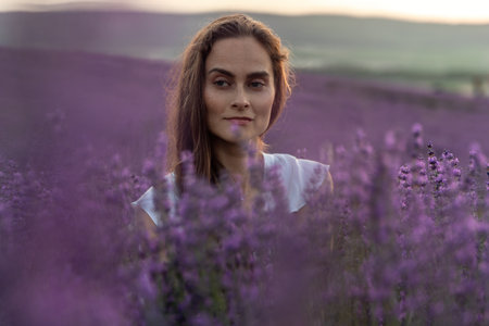 Close up portrait of happy young brunette woman in white dress on blooming fragrant lavender fields with endless rows. Warm sunset light. Bushes of lavender purple aromatic flowers on lavender fields.の写真素材