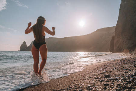happy carefree sensual woman with long hair in black swimwear posing at sunset beach. silhouette of...