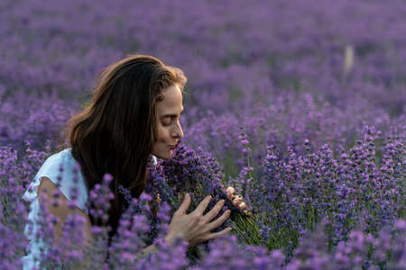 Close up portrait of happy young brunette woman in white dress on blooming fragrant lavender fields...